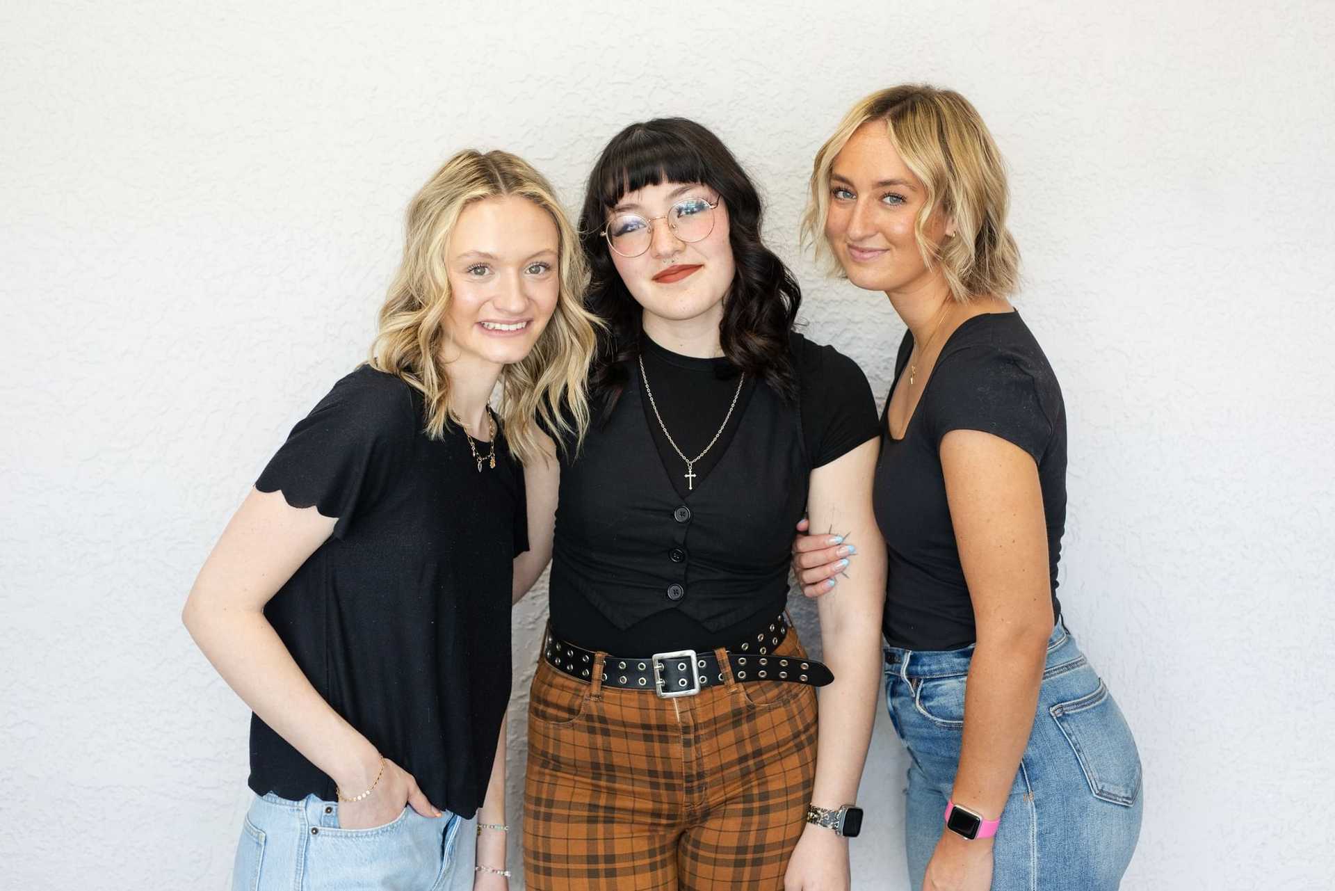 Three women in casual outfits smiling against a white background.