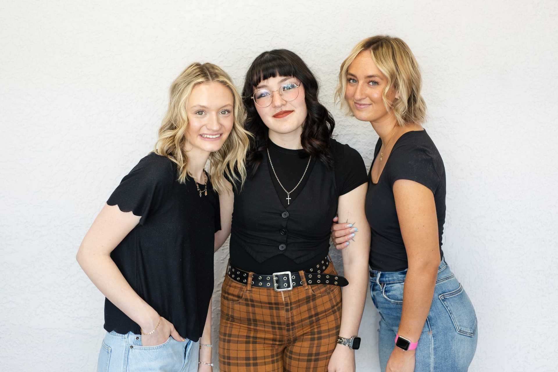 Three women in casual outfits smiling against a white background.