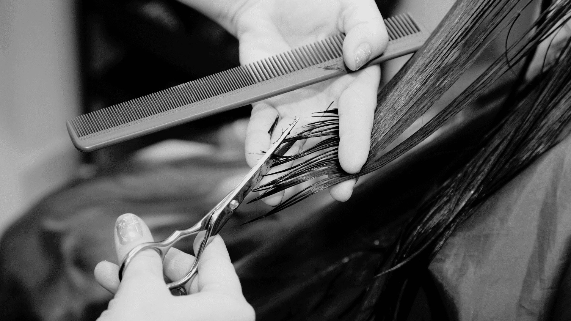 Hands trimming hair with scissors and comb in a hair salon.