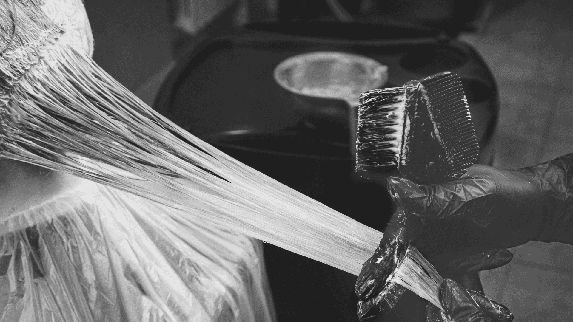 Hairdresser applying color to hair with a brush, hair covered in plastic wrap.