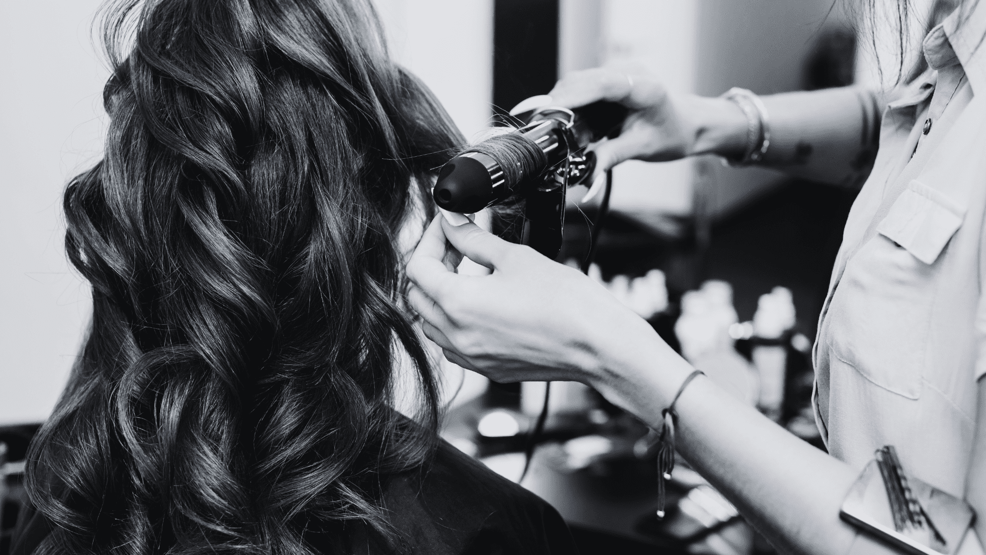 Woman getting curled hair styled at a salon by a stylist.