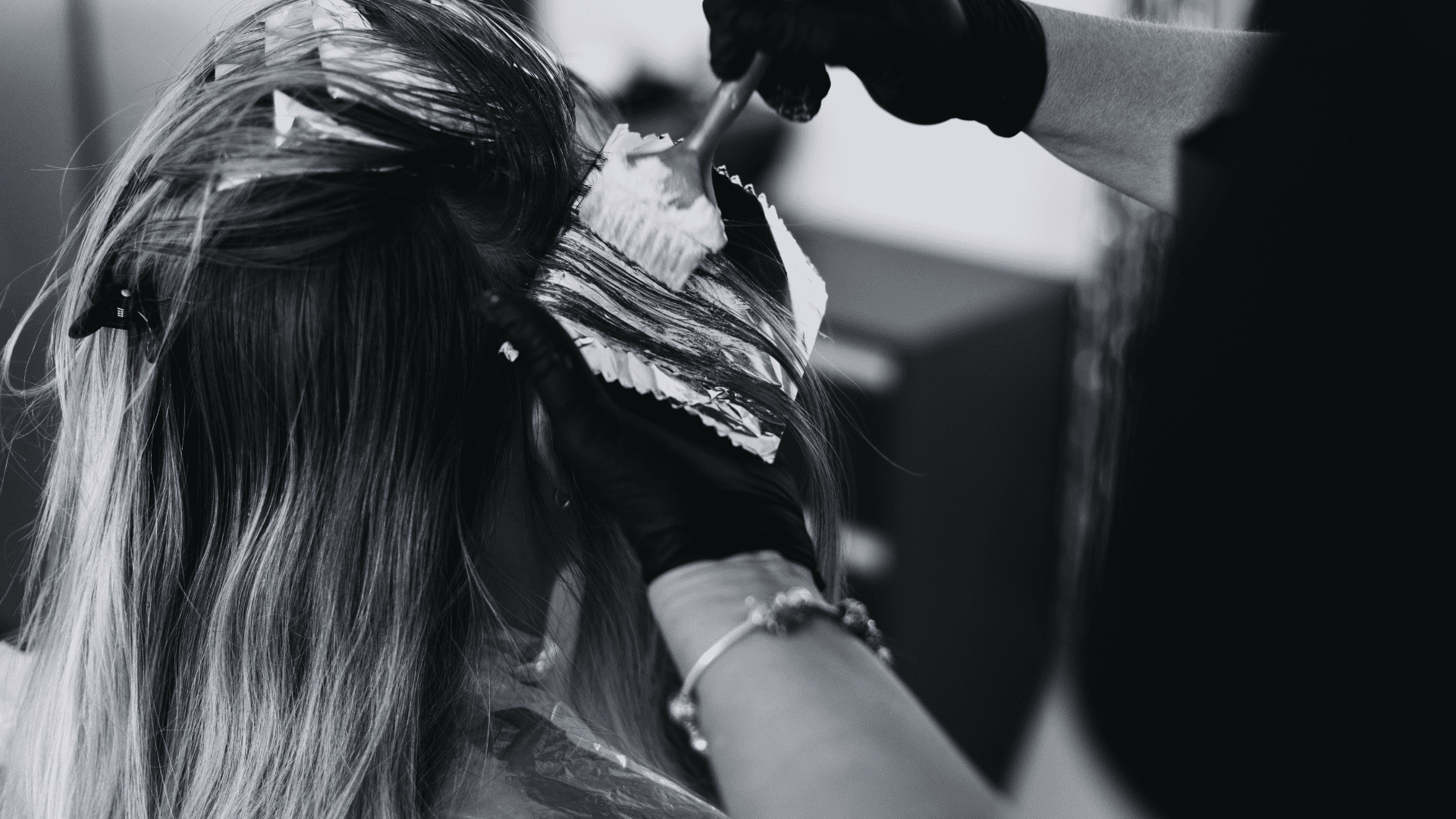 Hairdresser applying hair dye to a client's hair with a brush in a salon.