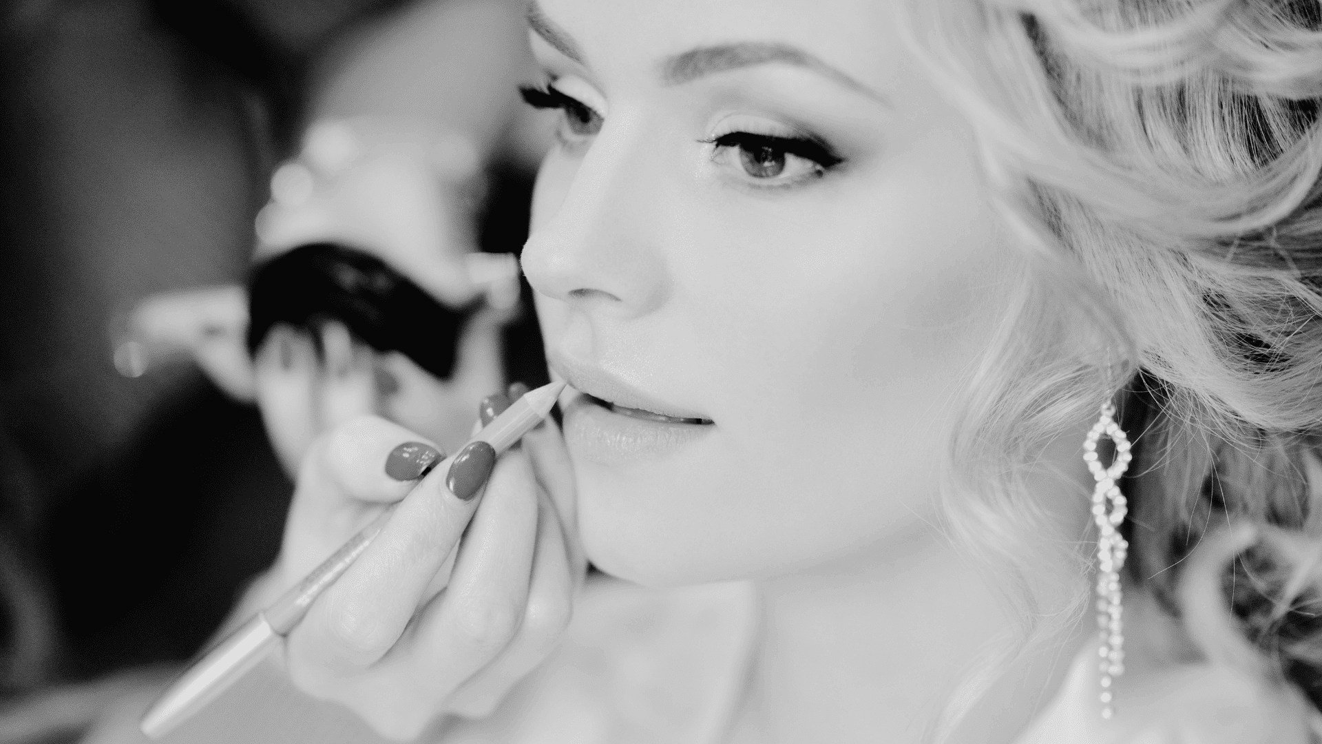 Woman having her lips carefully applied with makeup, wearing long earrings.